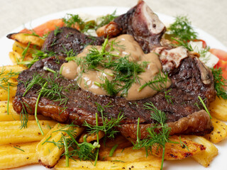 Dinner with premium t bone steak, fried potatoes chips with ridge, fresh salad with feta cheese on white plate and light color table cloth. Large portion of food with high quality products.