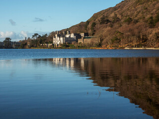 Obraz premium View on Kylemore Lough and Abbey in County Galway, Ireland. Major tourist attraction and landmark location. Blue cloudy sky and brown color winter mountain color. Travel and tourism