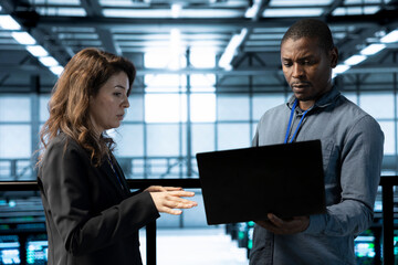 Data center programmer and colleague using laptop, conducting security audits, preventing errors....