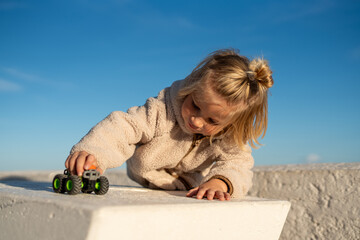 Happy Child Playing with a Toy Monster Truck on a White Concrete Surface Under a Clear Blue Sky.. © sutulastock