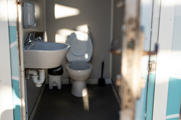 Open Door of a Public Restroom with Sink and Toilet in Natural Sunlight