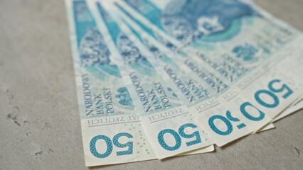 Polish banknotes of 50 zloty are spread out on a concrete surface showcasing various denominations.