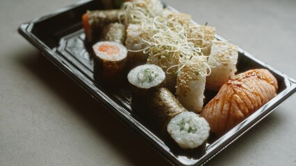 Sushi platter with various rolls and nigiri presented on a black plastic tray, placed on a concrete surface under natural light, showcasing a delicious and fresh assortment of japanese cuisine