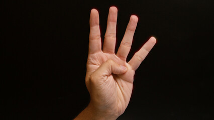 Man showing four fingers against a dark background, emphasizing the number four with his hand gesture.