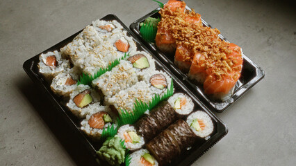 Fresh sushi rolls in black containers arranged on a gray surface, showcasing a variety of ingredients including avocado and salmon, perfect for a japanese cuisine themed meal.
