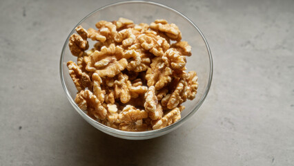 Bowl of raw walnuts on a light gray surface, showcasing healthy, nutritious, organic, shelled, and fresh nuts in a glass container, perfect for cooking, snacks or baking