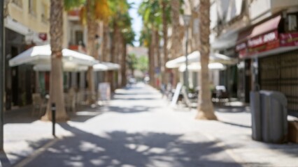 Fototapeta premium Blurred city street with defocused outdoor cafes and palm trees under bright sunlight