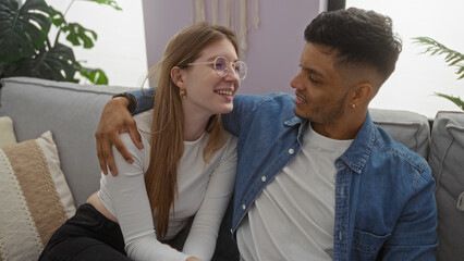 Couple sitting together on couch at home, woman and man sharing love and happiness in cozy living room with modern decor.