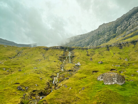 Mystical mountain landscape of lush green grass-covered mountains. The peaks are covered in low wispy clouds and fog. Kunoy, Faroe Islands, Kingdom of Denmark.