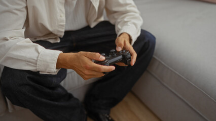 Young man playing video games in a living room using a game controller, focusing on his hands as he sits on a couch in a relaxed indoor setting