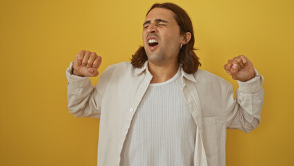 Young, hispanic man with long hair yawning over an isolated yellow background, expressing tiredness...