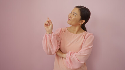 Woman pointing upward isolated over pink wall, young adult chinese female in stylish attire...