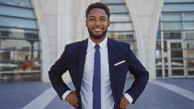 Handsome young african man in a suit smiling confidently standing outdoors in an urban city street environment
