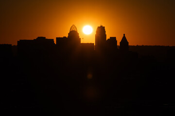 Fototapeta premium Sunrise over Cincinnati downtown city skyline with silhouettes of buildings and warm orange hues