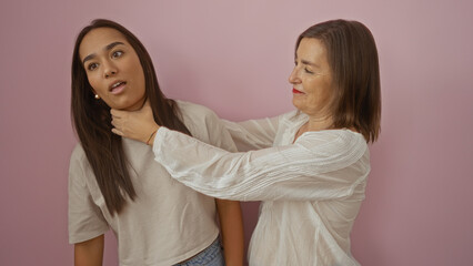 Mother playfully chokes daughter over isolated pink background, women smiling and sharing a fun, teasing moment, showcasing family love, humor, and connection.