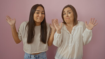 Mother and daughter posing together with a perplexed expression over an isolated pink background,...