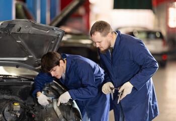 Two auto mechanics work together to diagnose an engine under the hood of a car in a repair shop