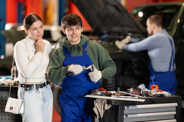Male mechanic advises young woman client on repairing under hood of car in car service station