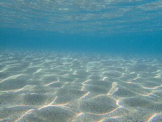 Dark blue ocean surface seen from underwater. Abstract waves underwater and rays of sunlight shining through, Sun light rays undersea deep, Underwater background with sea bottom, Mediterranean sea.