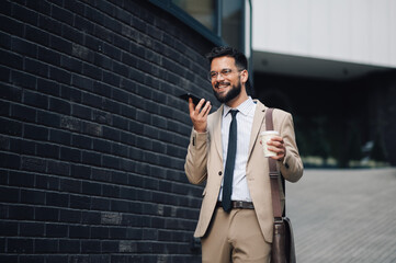 Businessman using smartphone walking with coffee outside office building