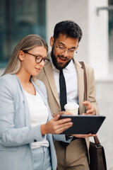 Business people having conversation about work on tablet outside office building