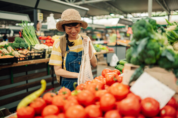 Young asian woman selecting tomatoes at bustling vegetable market.