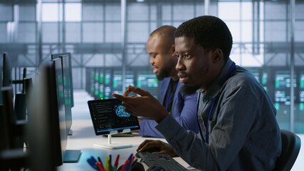 Cheerful coworkers in data center implementing AI predictive maintenance systems. Server room engineers using artificial intelligence to identify hardware failures impacting operations, camera A