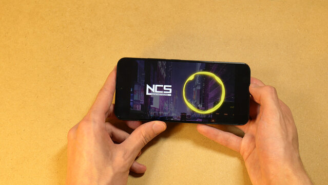 NoCopyrightSounds channel brand free music for creators, smartphone screen, hands holding a mobile device, playing an NCS YouTube video, royalty-free soundtrack sources