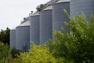 Silos at site of food products factory with trees in foreground, UK © Silent Corners