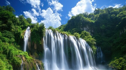 Fototapeta premium Lush Waterfall Cascading Down Mountainside, Sunny Sky