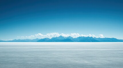 Fototapeta premium Serene landscape of a vast salt flat with distant mountains under a clear blue sky