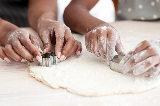 Closeup of afro-american family mother and daughter hands making diverse figures with cookie cutters, black mom and kid baking together at home, using biscuit figurines, baking concept