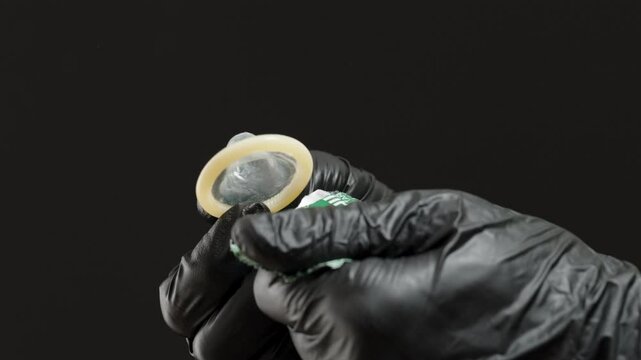 A Hand in Black Gloves Carefully Removing a Condom from Its Packaging, Demonstrating Proper Technique and Hygiene