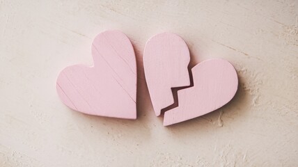 Fototapeta premium Two pastel pink wooden hearts, one whole and one broken, symbolizing love and heartbreak in a serene and minimalist setting.