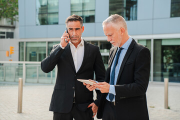 Two Businessmen are Actively Engaged in Important Conversations. One is Talking on the Phone While the Other is Reviewing Data on a Tablet. Essence of Professional Collaboration and Communication