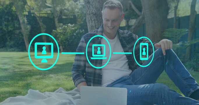 Image of network of connections with icons over caucasian man using laptop in park - Powered by Adobe