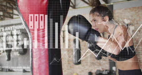 Image of diagrams and data processing over caucasian woman punching boxing bag at gym
