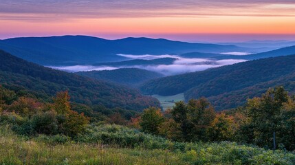 Obraz premium A serene mountain scene at dusk, with the sky glowing in shades of orange and purple, and mist settling in the valleys below.