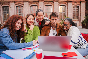 Enthusiastic Students Collaborating on a Laptop While Studying Together and Sharing Ideas in a Bright and Engaging Learning Environment Surrounded by Friends and Classmates at Their University Campus