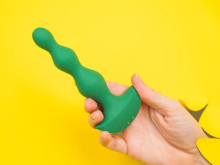 Female hand with green anal plug sticking out of yellow paper background.