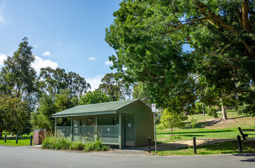 An old-fashioned public amenities or toilet building in a well-maintained and landscaped park, with...