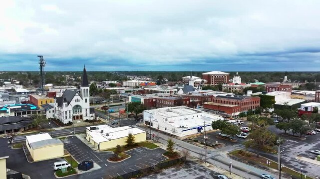 Cars on junction of Valdosta Town in Georgia during cloudy day. Red brick Buildings in downtown and white church., Aerial establishing wide shot.