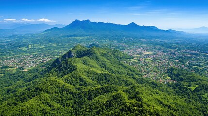 Obraz premium Aerial view of lush green mountains and valleys under a clear blue sky with distant peaks