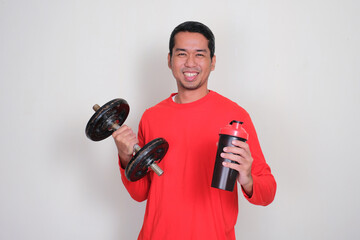 A sporty man smiling happy while holding dumbbell and drink tumbler