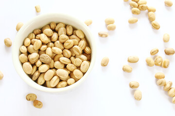 Carioca beans in a bowl and grains scattered on the white background.