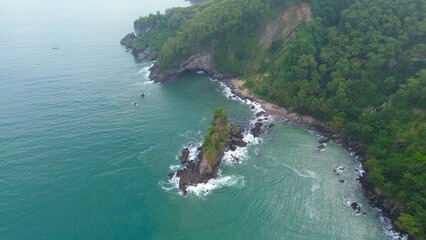 Aerial drone view of the coastline and seashore with rocks, hills and trees, beach sand and waves from the ocean at Karang Agung Beach, Kebumen, Central Java, Indonesia