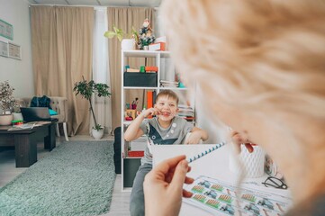 boy smiling and look at camera with speech therapy exercises in a bright educational office with a female therapist, concept of childhood development, education