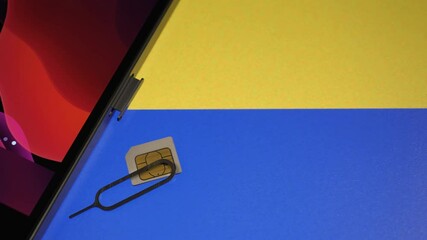 Smartphone and a sim card with the Ukrainian flag in the background. Communication during the war. Some companies provide free calls to Ukraine. Camera slowly moving sideways. Closeup. Text space. - Powered by Adobe