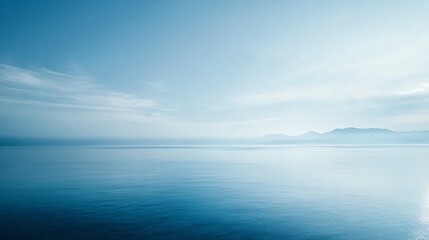 Fototapeta premium Serene blue seascape with distant mountains and a calm, cloudy sky