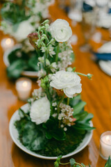 Elegant white floral arrangement displayed on a wooden dining table for a special event with candles
